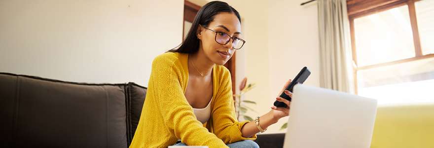 Young woman looking at a phone and laptop